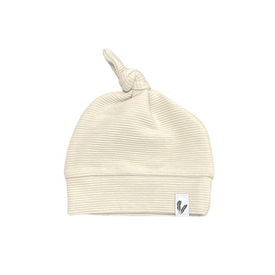Beige knoopmutsje in ribstof met brede omslag en een wit label met veertjes.