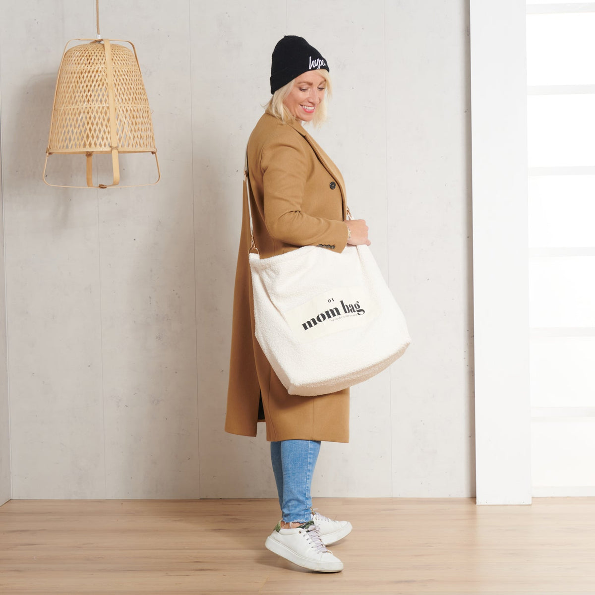 Vrouw met een ivoorkleurige Mom Bag Teddy Bouclé over haar schouder, gedragen bij een camelbruine jas.