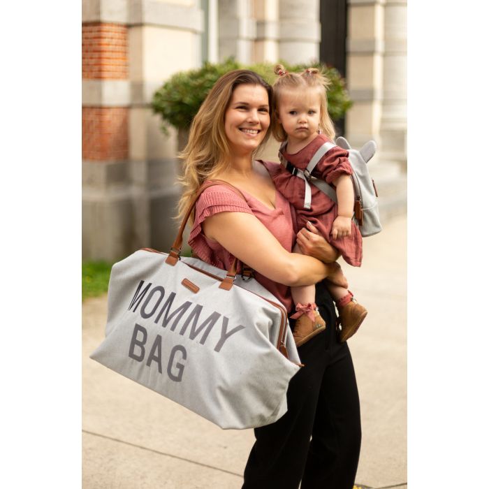 Vrouw met een kind op de arm en een grijze Mommy Bag verzorgingstas over haar schouder.