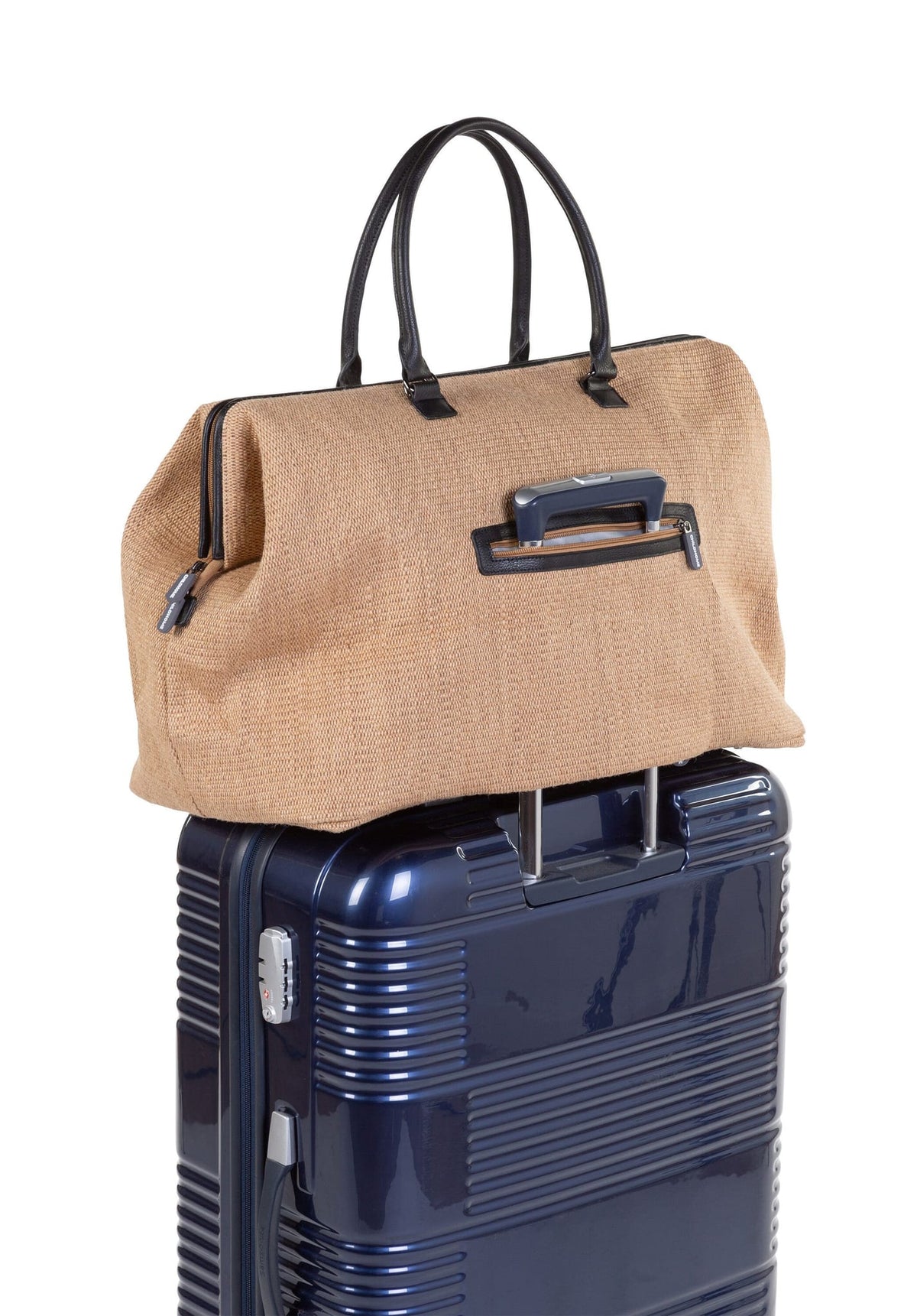 Achterkant van de Mommy Bag verzorgingstas met raffialook, bevestigd aan de trekstang van een blauwe koffer.