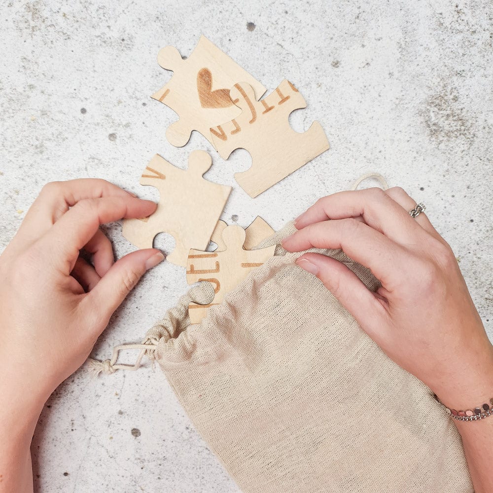 Handen halen houten stukjes van de puzzel ‘Wij krijgen een baby’ uit een beige linnen zakje.