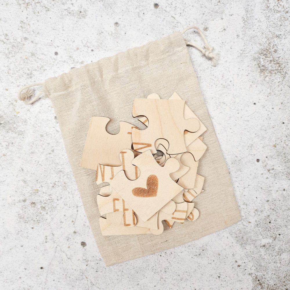 Losse houten puzzelstukjes met letters en een hartje op een beige linnen zakje.