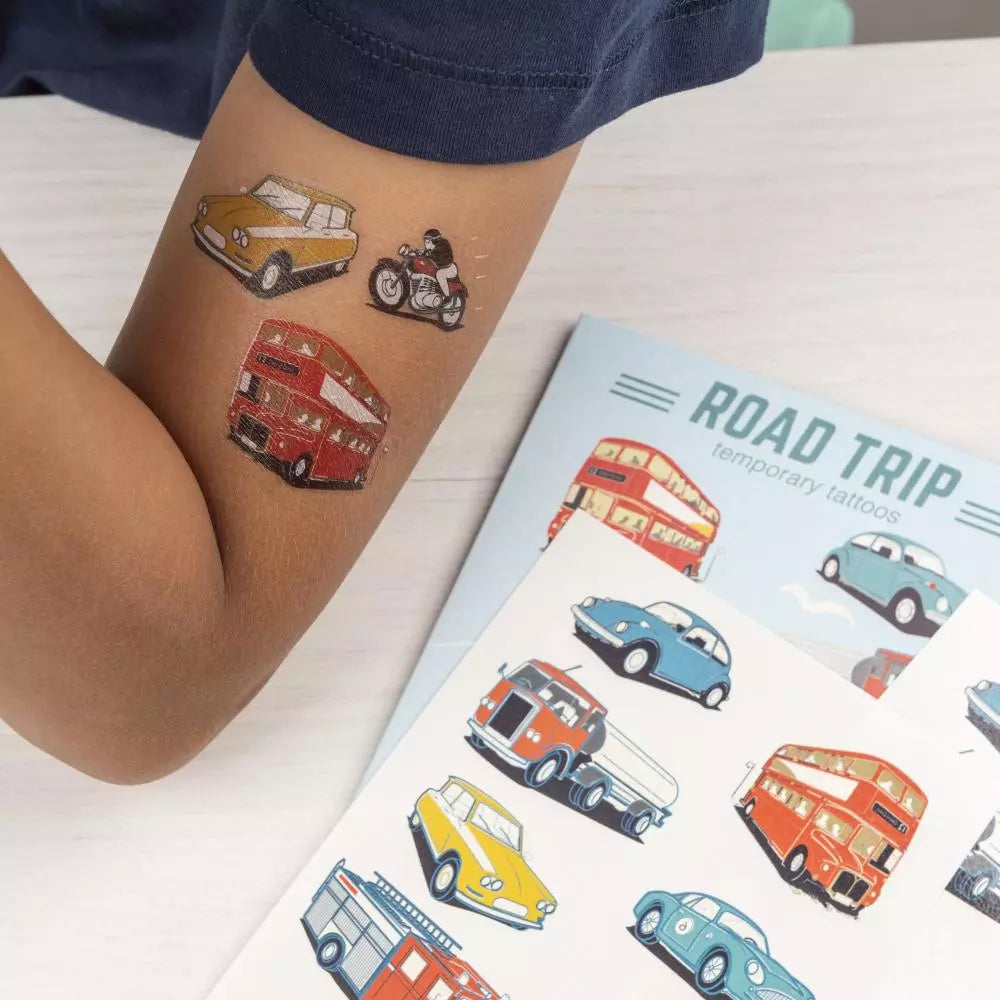 Voertuigentattoos van een gele auto, motor en rode dubbeldekker op een kinderarm, naast de verpakking en een vel tattoos.