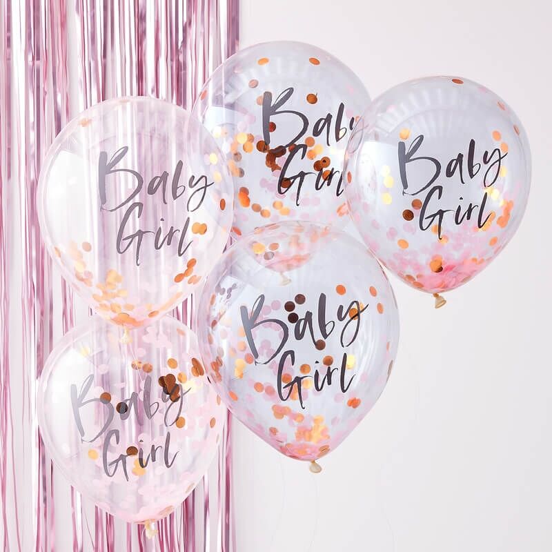 Vijf transparante ballonnen met 'Baby Girl' en roze en goudkleurige confetti voor een roze franjesachtergrond.