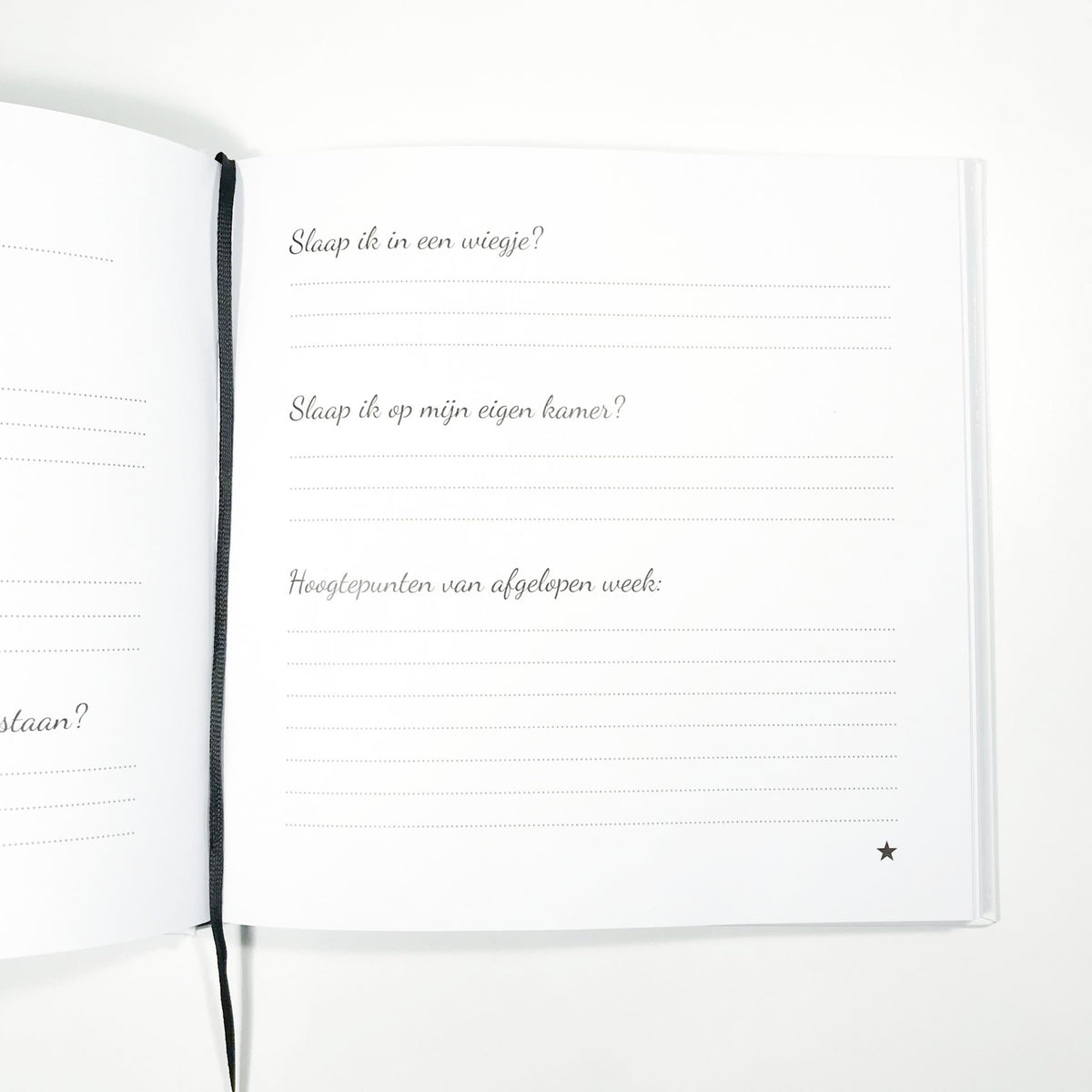 Open babyboek met vragen over slapen en hoogtepunten van de afgelopen week, naast een zwart leeslint.
