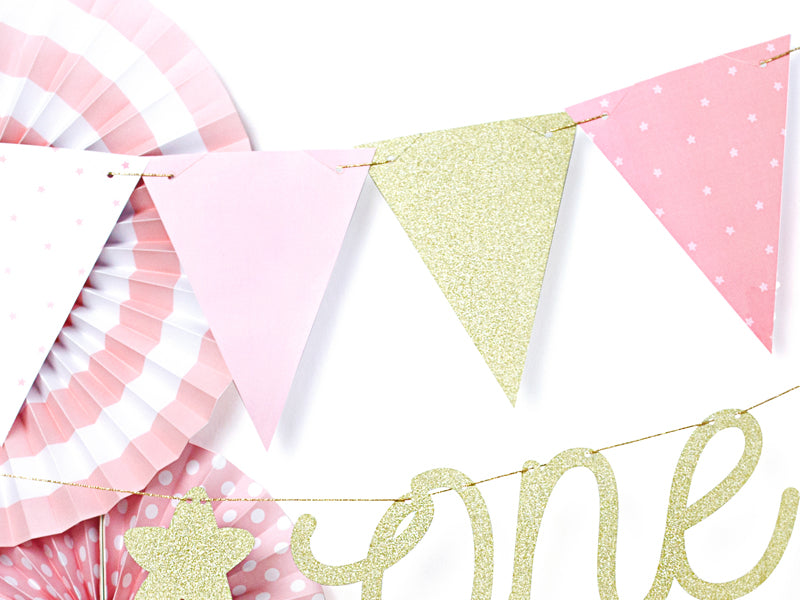 Roze slinger met goudkleurige glittervlaggetjes, gecombineerd met papieren waaiers en een goudkleurige letterslinger.