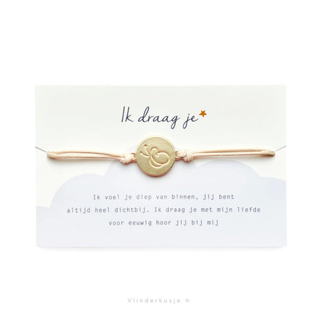 Armbandje Ik Draag Je met lichtroze koord en goudkleurige ronde vlinderbedel op een kaartje met gedicht.