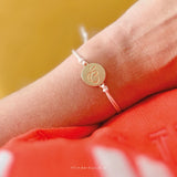 Detail van het armbandje met lichtroze koord en goudkleurige vlinderbedel om een pols boven rode kleding.