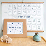 Baby Mijlpalen Bingo met blauwe pictogrammen aan houten ophanglatten, met de bruine enveloppe ervoor.