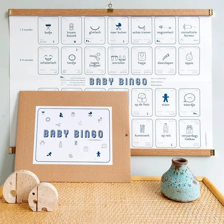 Baby Mijlpalen Bingo met blauwe pictogrammen aan houten ophanglatten, met de bruine enveloppe ervoor.
