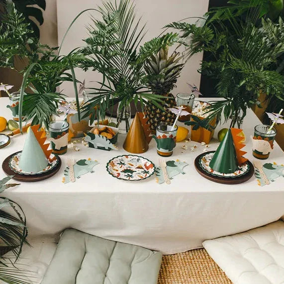 Feesttafel met glazen met dinowikkels, dinosaurusbordjes, feesthoedjes en veel groen.