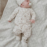 Baby met speen in boxpakje Dried Flowers met bijpassend mutsje en gebreide slofjes, liggend op een deken.