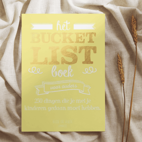 Geel Bucketlist Boek voor ouders op een lichte doek, naast gedroogde graanhalmen.