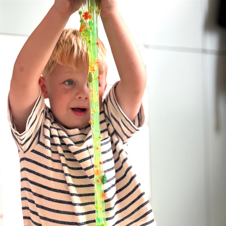 Een kind houdt Dino Dew-slijm boven het hoofd en rekt het uit tot een lange, dunne groene sliert met bedeltjes.