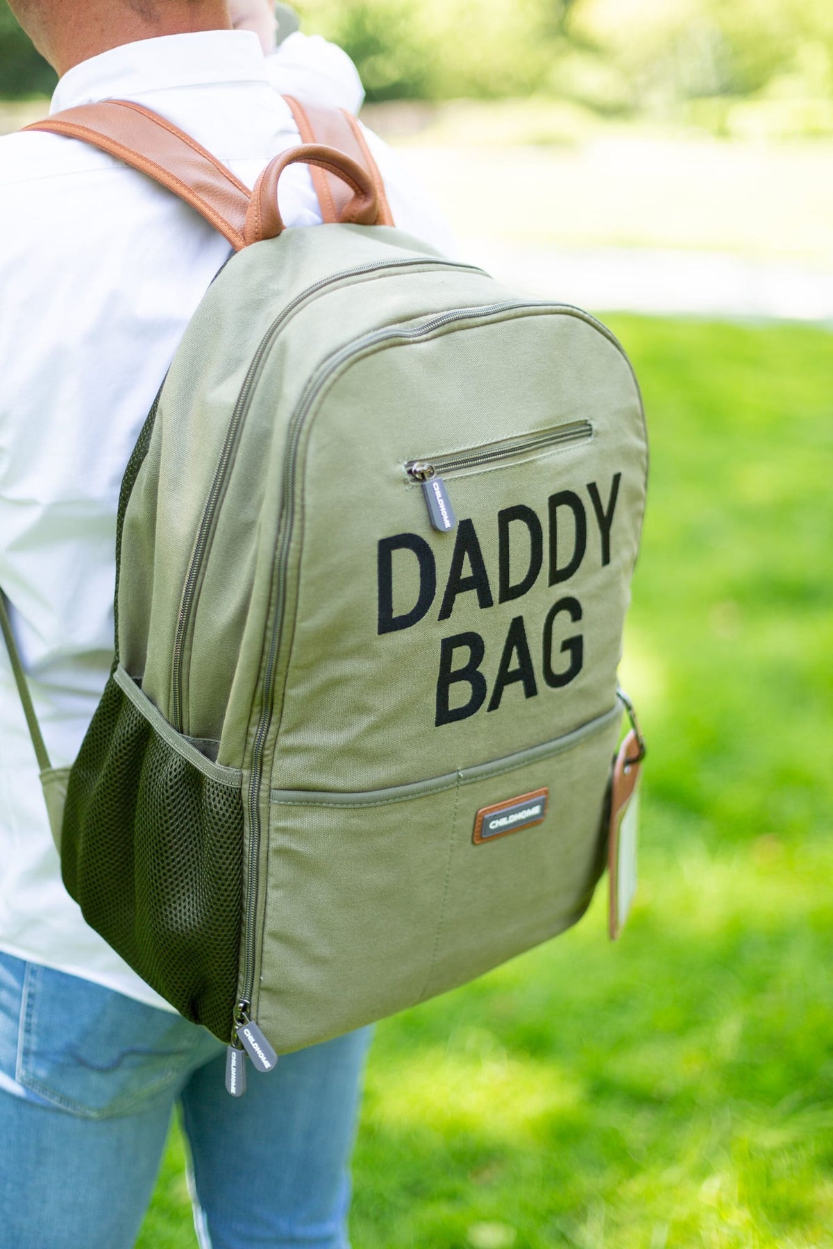 Kaki Daddy Bag verzorgingsrugzak met zwarte letters en bruine schouderbanden, buiten gedragen op de rug.
