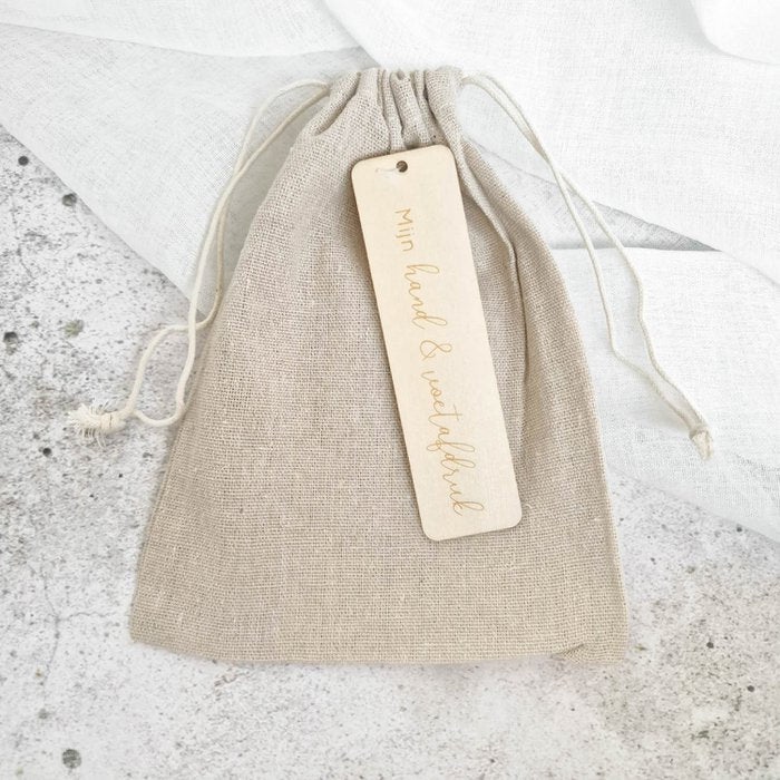 Gesloten beige linnen bewaarzakje met trekkoord en label ‘Mijn hand & voetafdruk’.