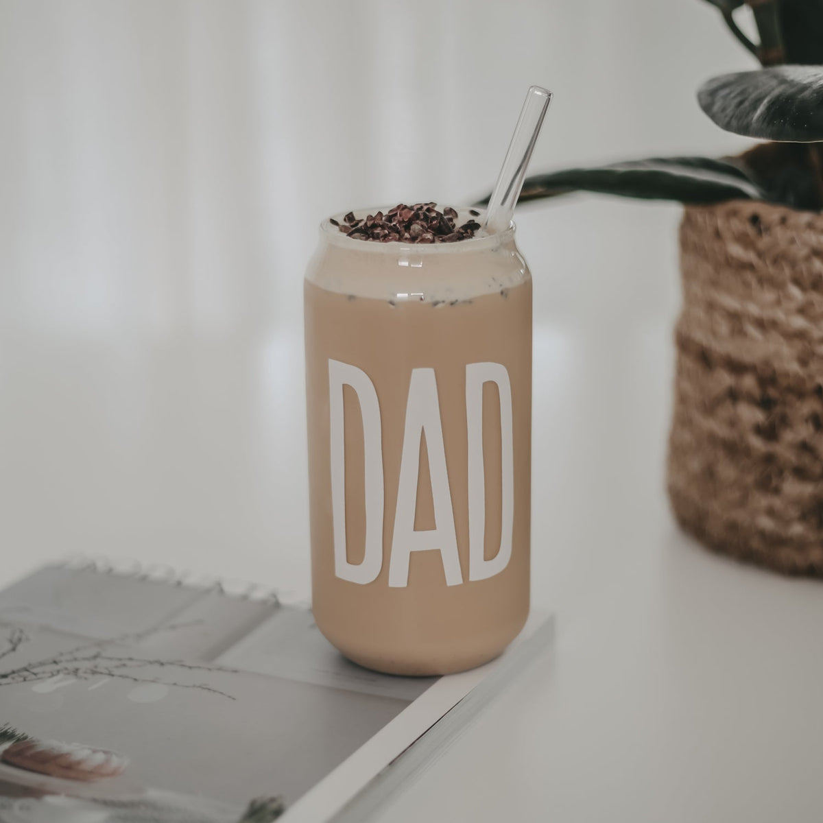 Hoog drinkglas met witte tekst ‘Dad’, gevuld met een lichtbruine drank met schuim en een transparant rietje.