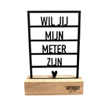 Zwart houten frame met de tekst ‘Wil jij mijn meter zijn?’ en een hartje, op een eiken blokstandaard.