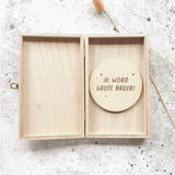 Open houten kistje met een houten cirkel met de tekst ‘Ik word grote broer!’ op een lichtgrijze ondergrond.