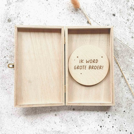 Open houten kistje met een houten cirkel met de tekst ‘Ik word grote broer!’ op een lichtgrijze ondergrond.