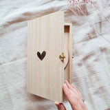 Een hand opent het houten kistje met gegraveerd hartje; binnenin is een houten cirkel deels zichtbaar.