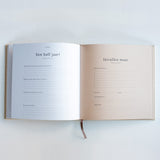 Invulboek Mijn Eerste Jaar met witte en lichtroze invulpagina’s over zes maanden, met onderaan een leeslint.