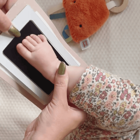 Babyvoetje op het zwarte inktpad van de kaartenset 'Mijn Handje & Mijn Voetje', ondersteund door een hand.