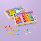 Open Today Is A Good Day-knikkersbox met kleurrijke knikkers en kiezelstenen, los verspreid op een paarse ondergrond.