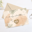 Kraskaart ‘Je wordt opa’ met groene bladeren en goudkleurig krashart op een envelop op een witte tafel.