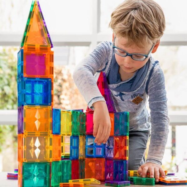 Kind met bril bouwt een kleurrijk kasteel met hoge torens van magnetische bouwblokken
