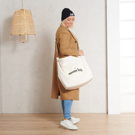 Vrouw met een ivoorkleurige Mom Bag Teddy Bouclé over haar schouder, gedragen bij een camelbruine jas.