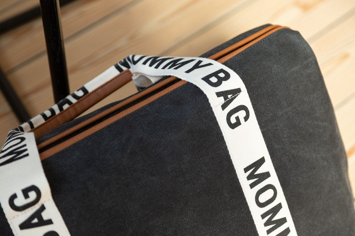 Detail van de zwarte Mommy Bag verzorgingstas met bruine ritssluiting en crèmekleurige draagband met opdruk.
