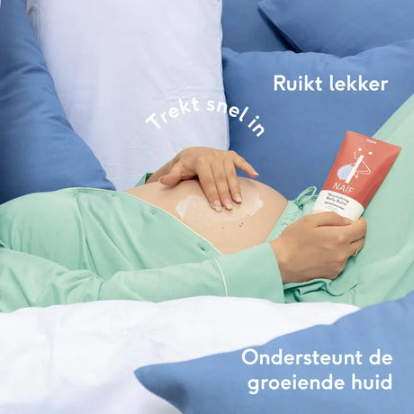 Zwangere vrouw smeert Naïf Nourishing Belly Balm op haar buik en houdt de rood-witte tube vast.