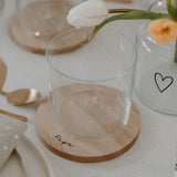 Ronde eiken onderzetter met handgeschreven opdruk 'Papa' onder een leeg glas op een gedekte tafel.