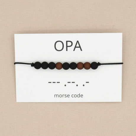 Opa-armband in morsecode met zwarte en bruine kralen aan een zwart koord, op een wit kaartje met ‘opa’ en morsecode.