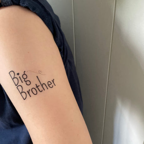 Plaktattoo ‘Big Brother’ in zwarte letters met hartjes op de bovenarm van een kind