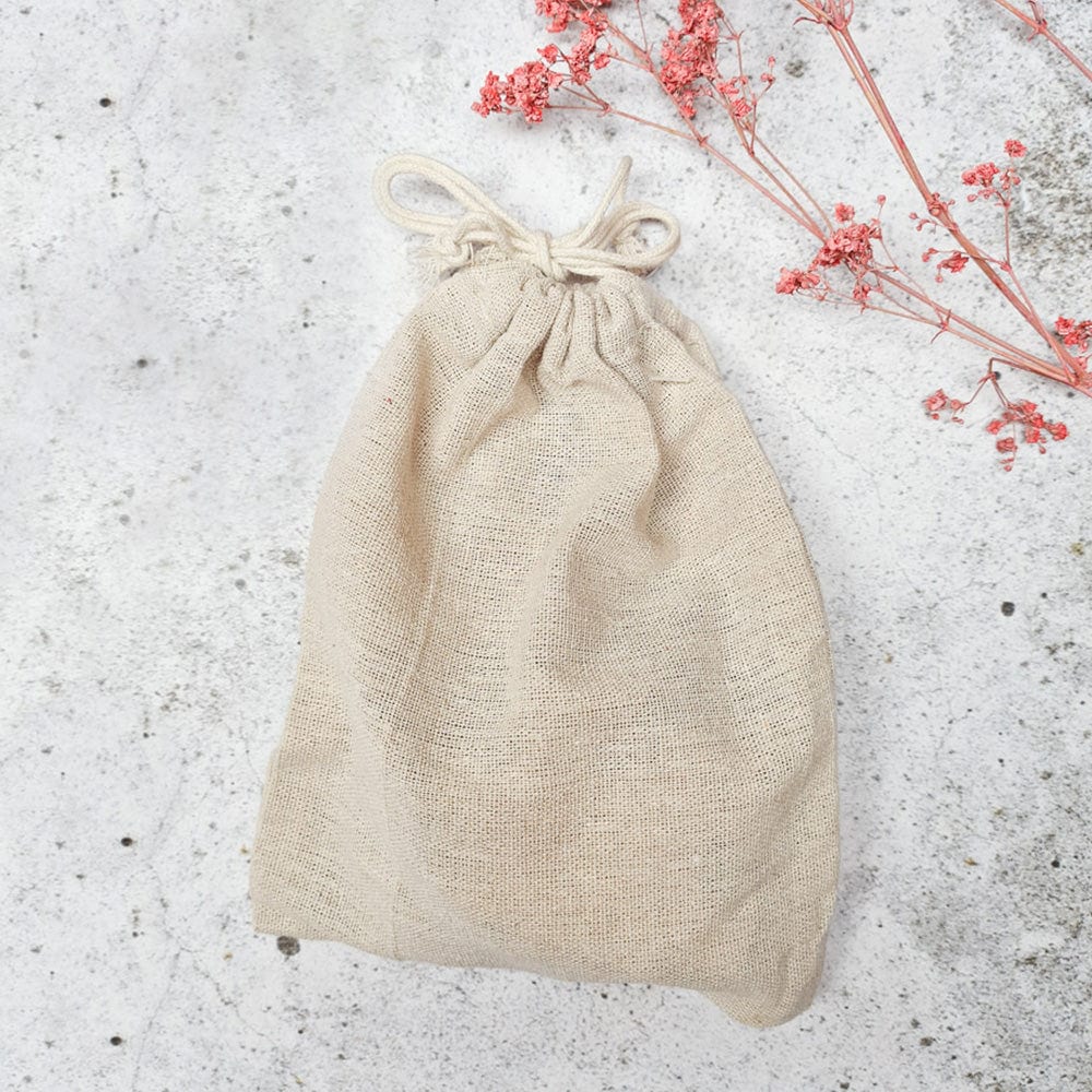 Gesloten beige linnen zakje met trekkoord voor de puzzel ‘Wij krijgen een baby’, naast roze droogbloemen.