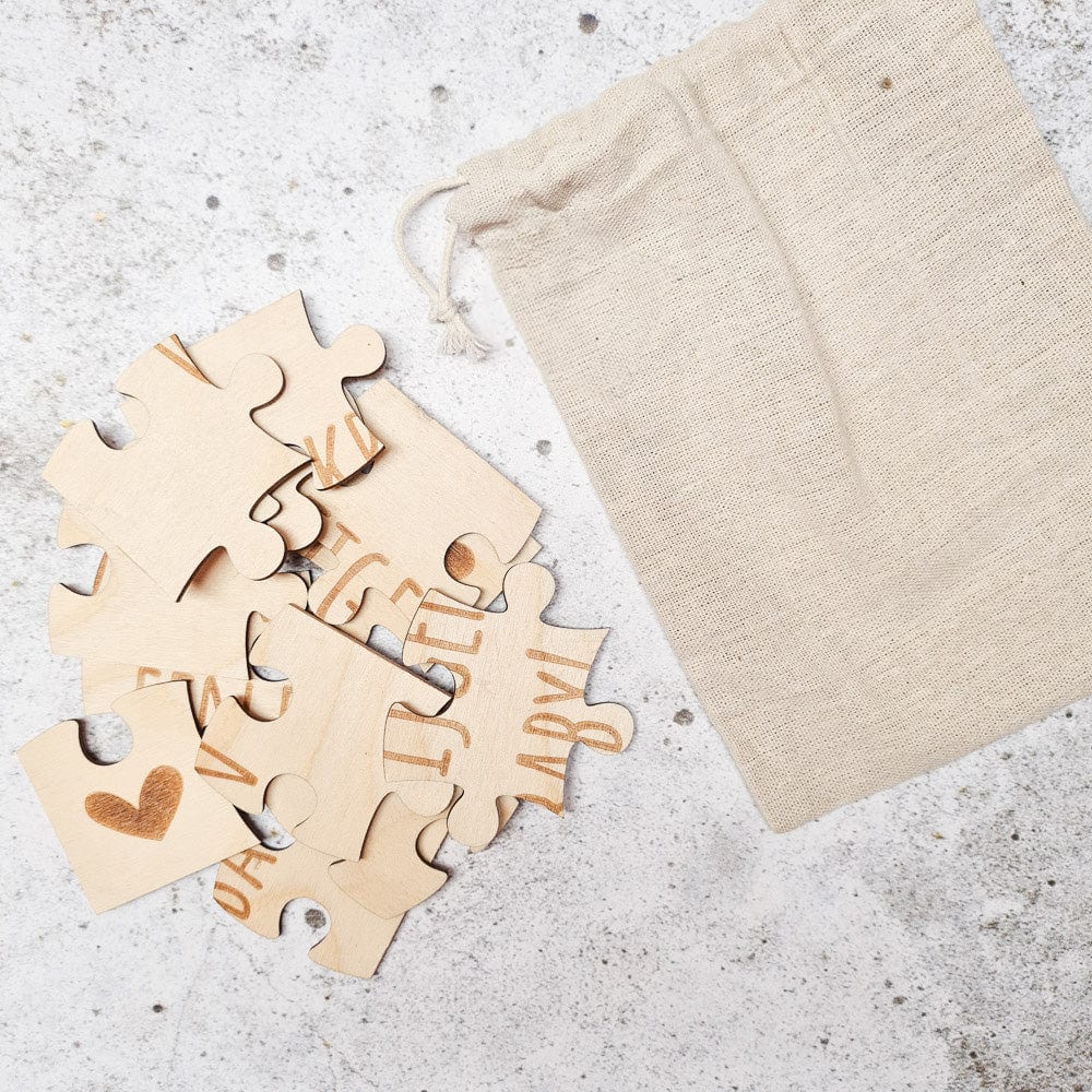 Houten stukjes van de puzzel ‘Wij krijgen een baby’ met een hartje en letters naast een beige linnen zakje.