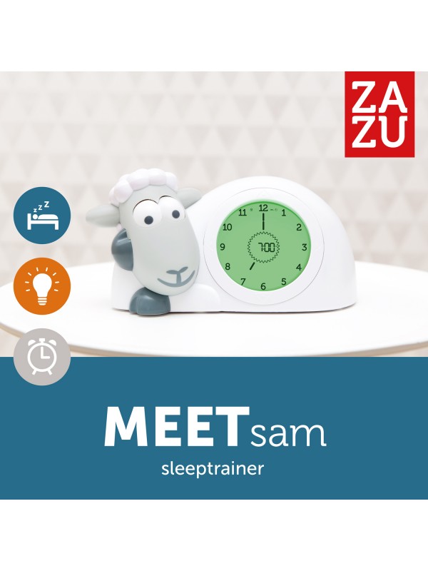 Grijze Zazu slaaptrainer Sam met open ogen en groene wijzerplaat op een witte tafel.