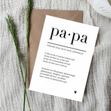Witte ansichtkaart Papa met zwarte tekst en een klein hartje, op een bruine envelop naast groene takjes.