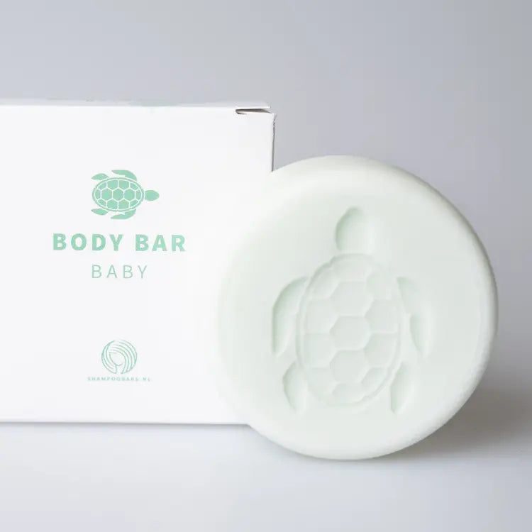 Lichtgroene Body Bar Baby met schildpadmotief naast een witte verpakking op een lichtgrijze achtergrond.
