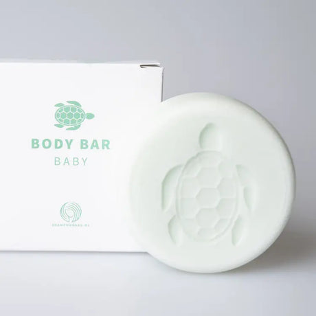 Lichtgroene Body Bar Baby met schildpadmotief naast een witte verpakking op een lichtgrijze achtergrond.
