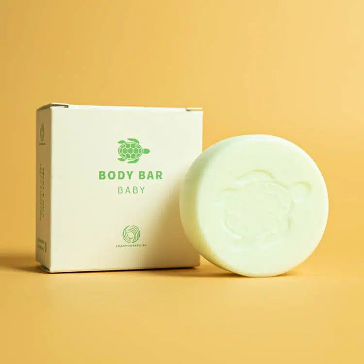 Lichtgroene Body Bar Baby met schildpadmotief naast de verpakking op een gele achtergrond.