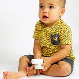 Zittend kind in een geel shirt met tijgerstrepen houdt twee ronde zeepbars vast, waaronder de lichtgroene Body Bar Baby.
