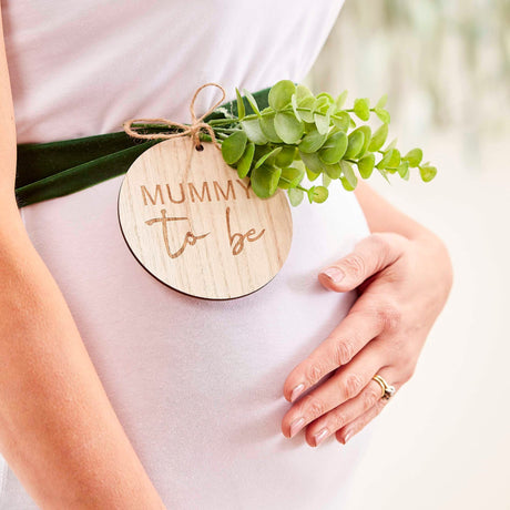 Donkergroene buiksjerp met houten badge ‘Mummy to be’ en groene blaadjes rond een zwangere buik.