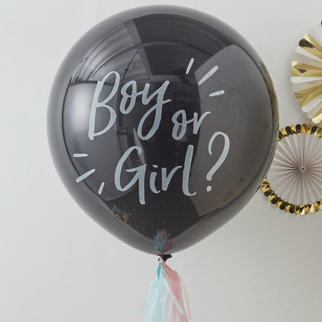 Zwarte gender reveal ballon met witte tekst ‘Boy or Girl?’, roze en blauwe kwastjes en papieren waaiers op de achtergrond