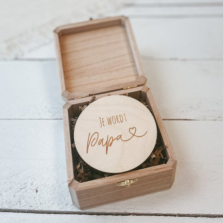 Ronde houten badge met ‘Je wordt papa’ en een hartje, in een open houten kistje met papieren opvulling.