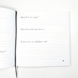 Open babyboek met vragen over slapen en hoogtepunten van de afgelopen week, naast een zwart leeslint.