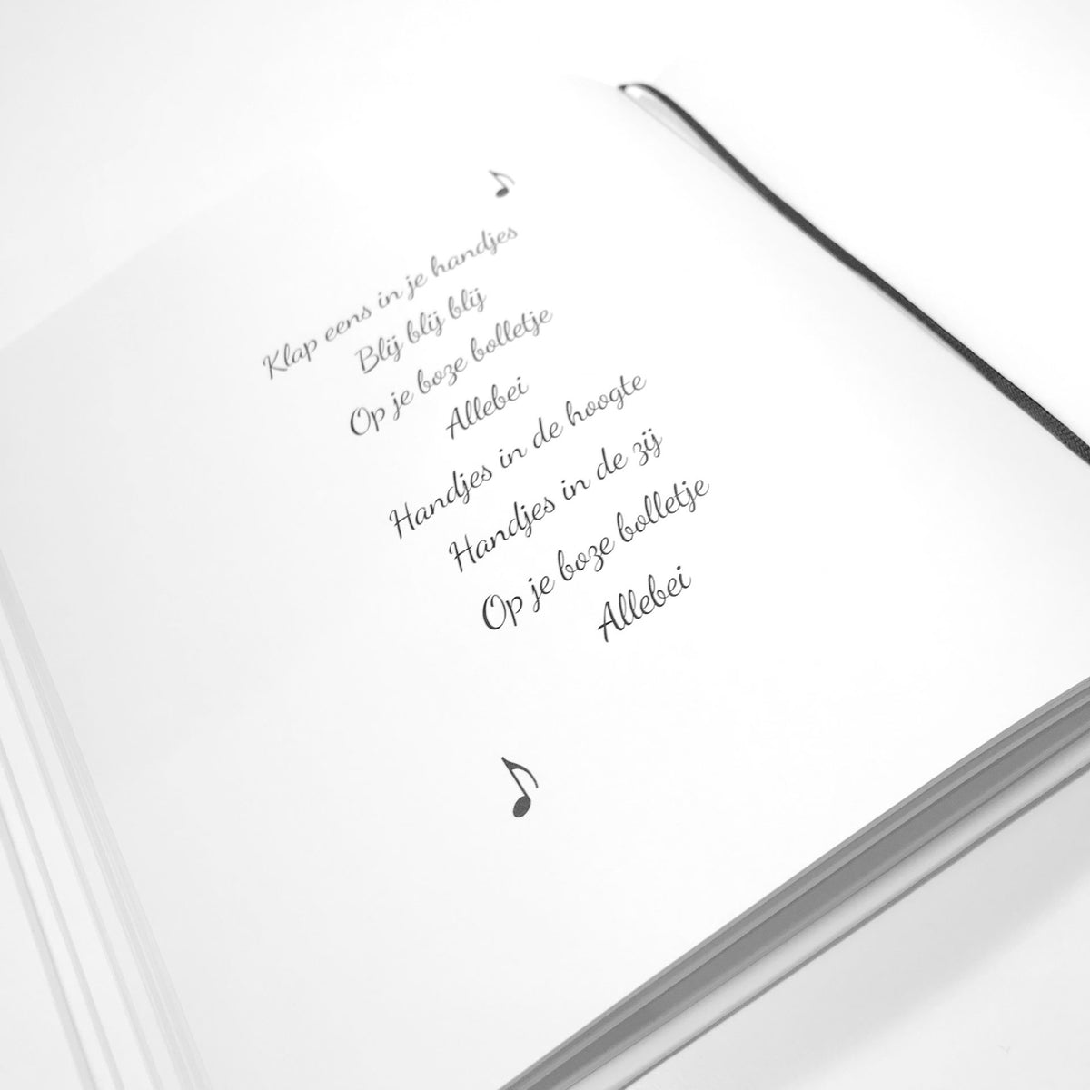 Pagina in het babyboek met het liedje Klap eens in je handjes, muzieknoten en een zwart leeslint.