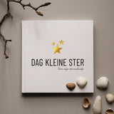 Invulboek Dag Kleine Ster met witte kaft en goudkleurige sterren, omringd door schelpen en een tak.